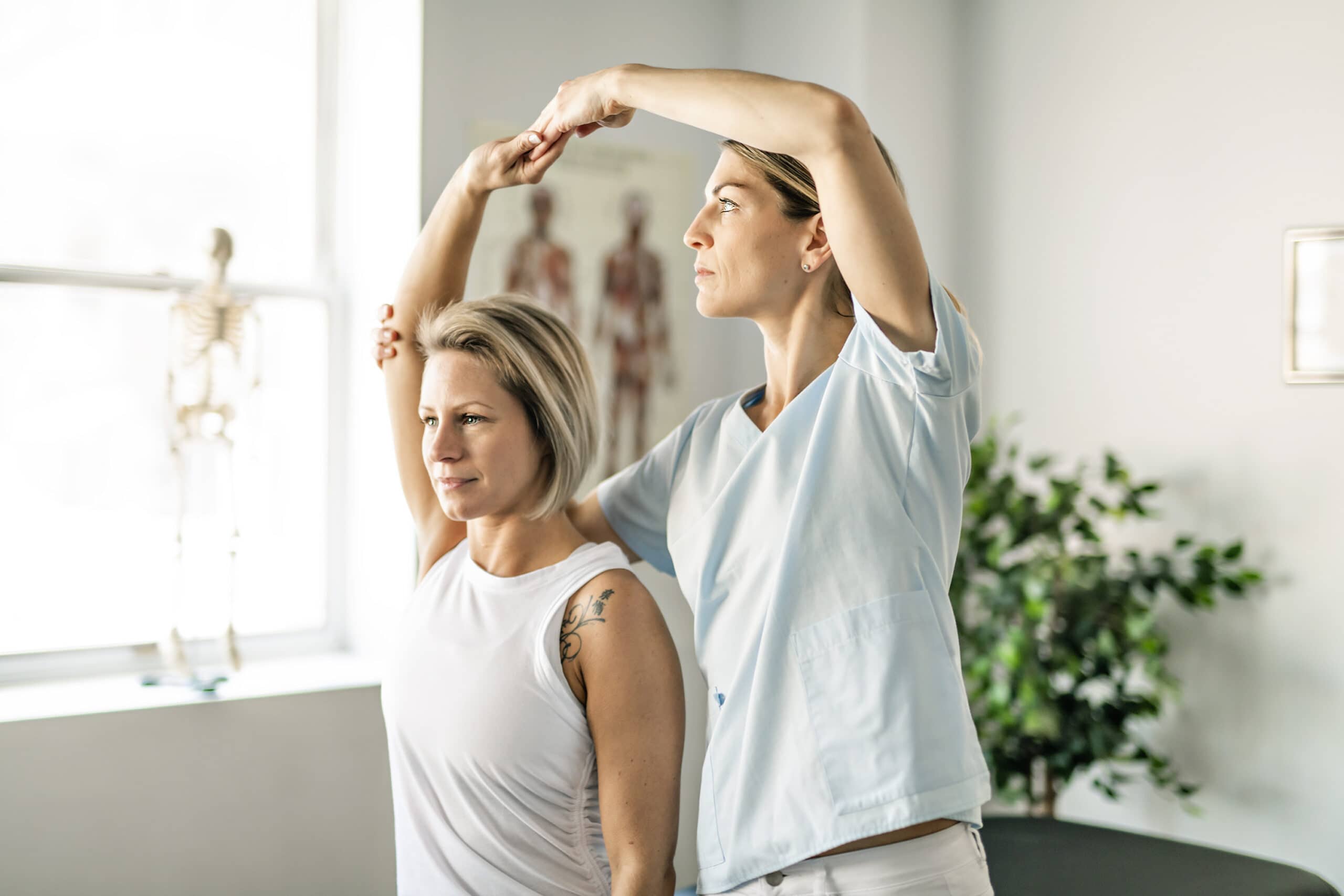 Assistante masseuse effectuant un étirement des bras d’une cliente assise, dans un espace de soins. (note: alt text integrates main keyword naturally if possible; here it's not forcing a keyword insertion since image shows a training/therapy scene rather than explicit text. If needed: "Démonstration de techniques de stretching liée à comment devenir massothérapeute" but keep natural.)