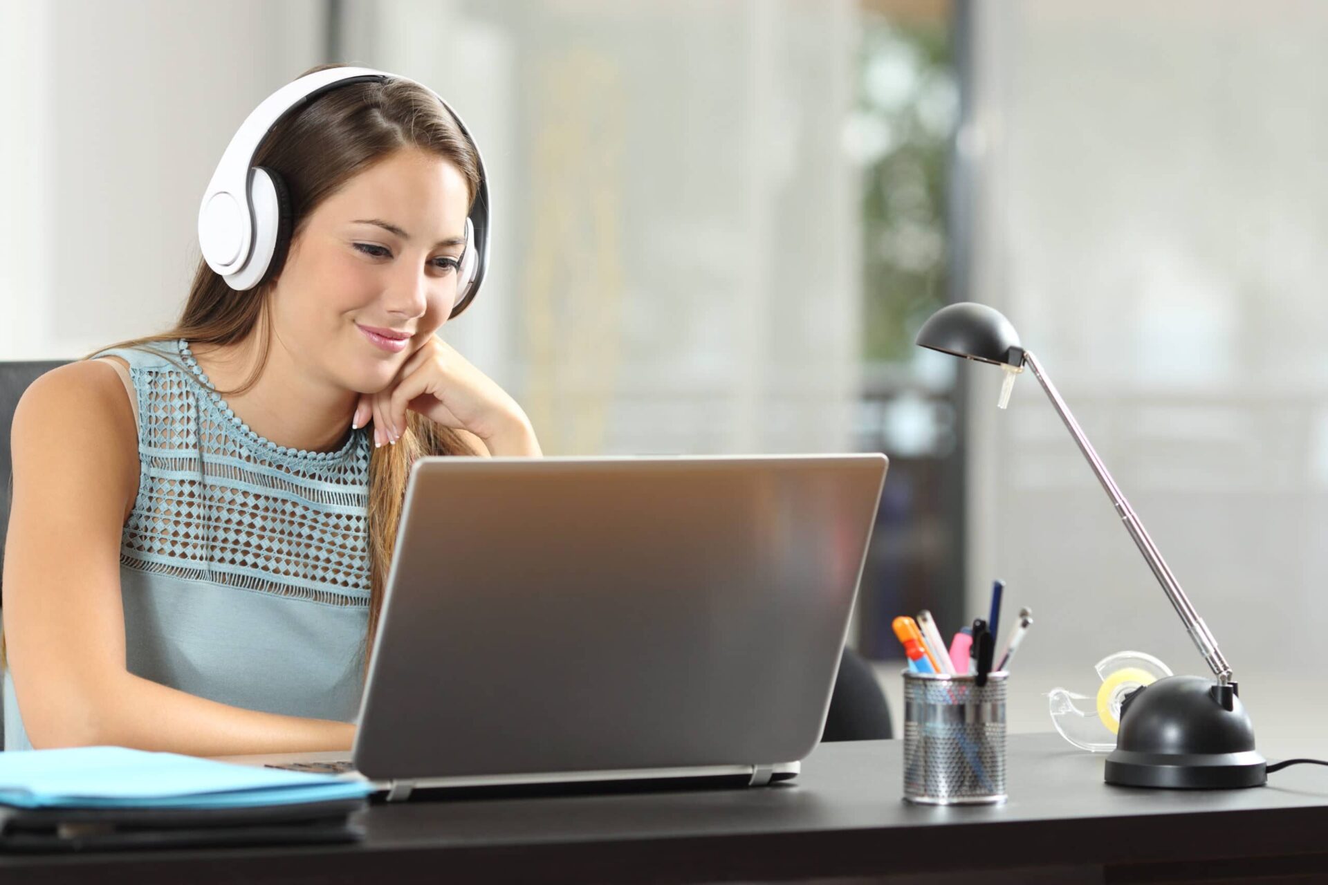 Étudiante souriante avec casques audio, travaillant sur un ordinateur portable dans un bureau climatisé. Étudiante souriante avec casques audio, travaillant sur un ordinateur portable dans un bureau climatisé.